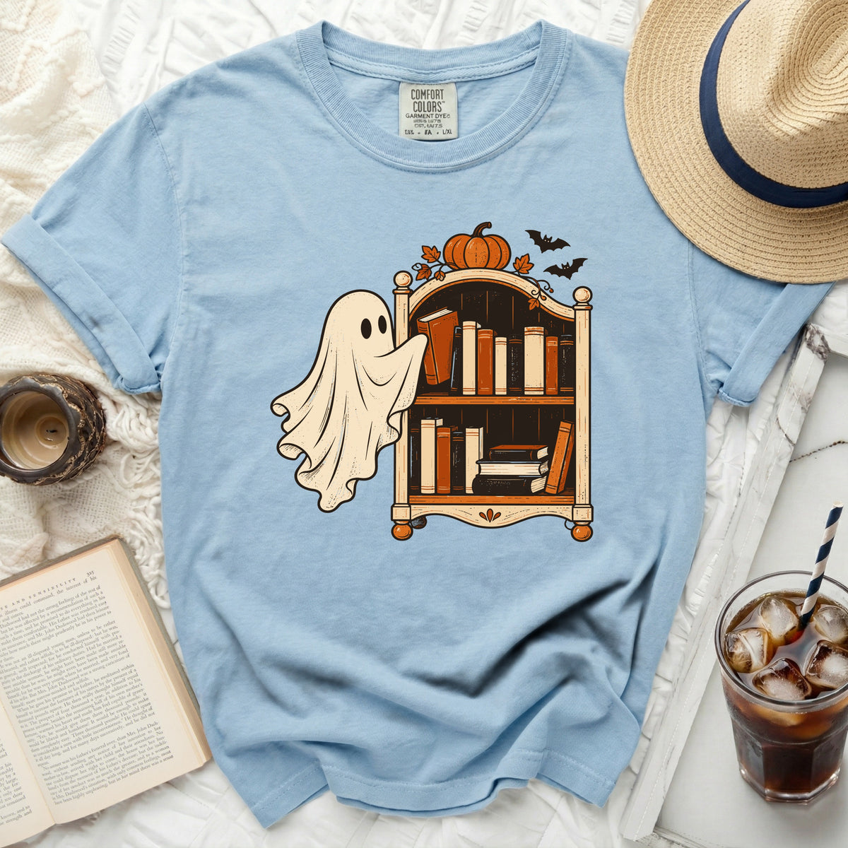 Light blue t-shirt with a ghost reaching for books on a shelf, featuring a pumpkin and bats.