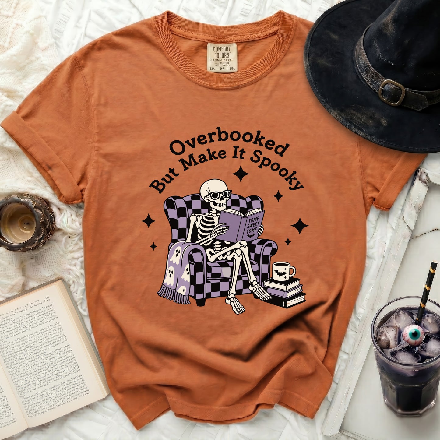 Orange t-shirt with skeleton reading a book. "Overbooked But Make It Spooky" text.