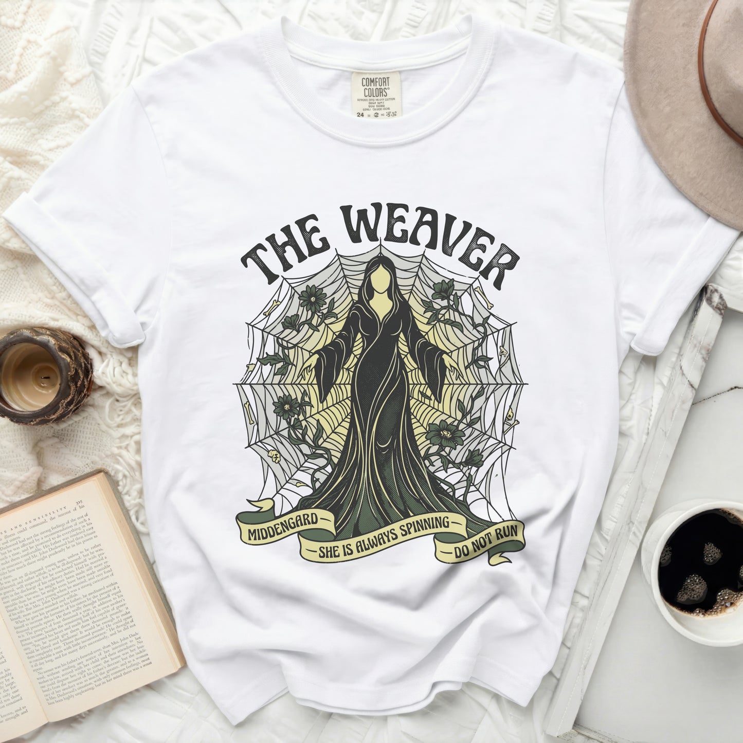 White t-shirt with "The Weaver" design, featuring a robed figure and spiderweb.