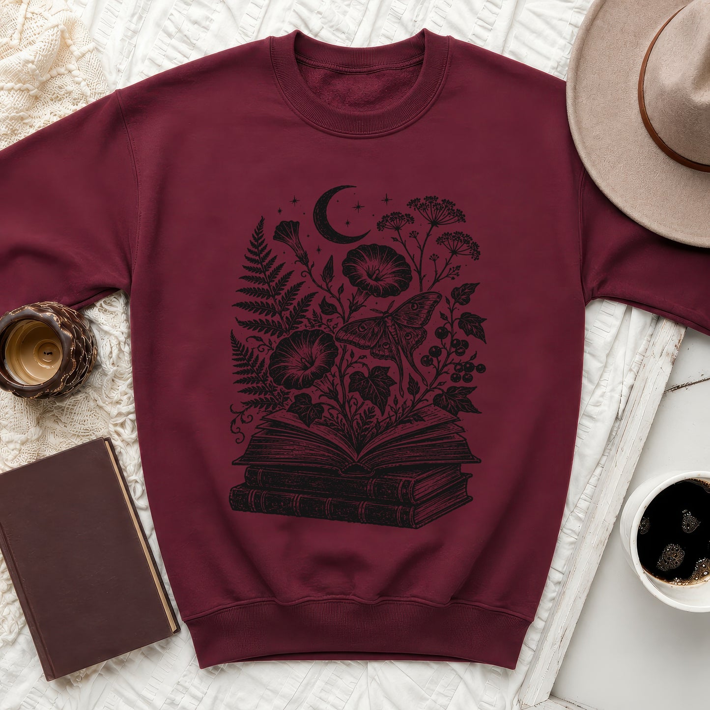 Maroon sweatshirt with black print of open book, moth, moon, and botanical elements.