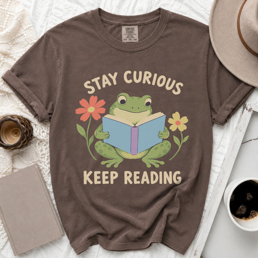 Brown t-shirt with a frog reading a book, surrounded by flowers and text.