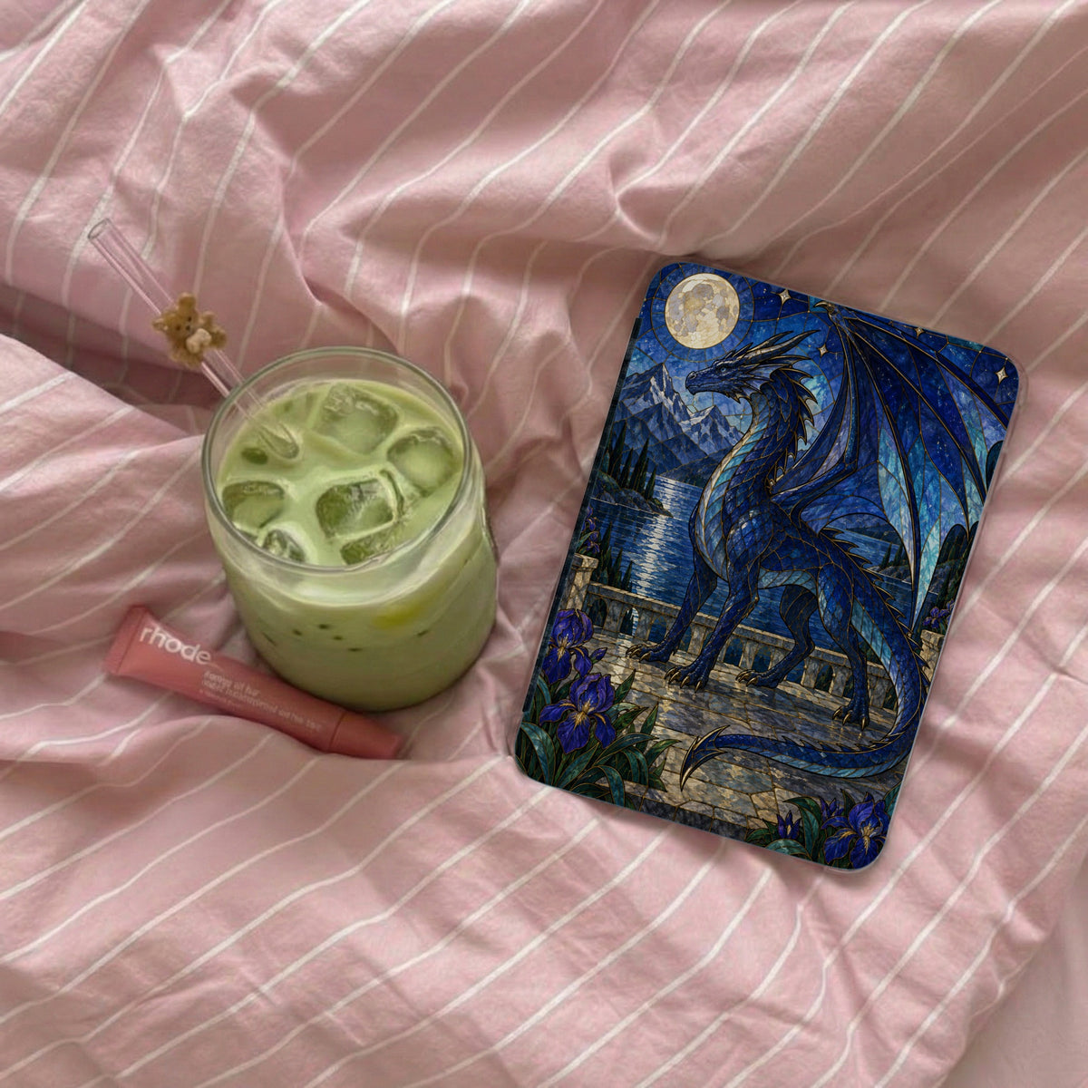 Blue dragon on stained glass design with moon and mountains beside iced green drink.