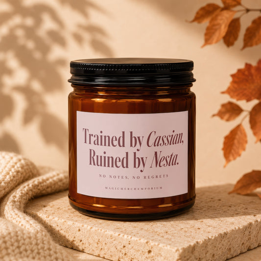 Amber glass jar candle with a black lid and a label reading Trained by Cassian, Ruined by Nesta.
