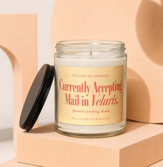 A glass candle jar with a black lid and a label reading "Currently Accepting Mail in Velaris."