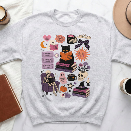 Grey sweatshirt with Halloween-themed graphic featuring books, a black cat, skeleton, and witchy elements.