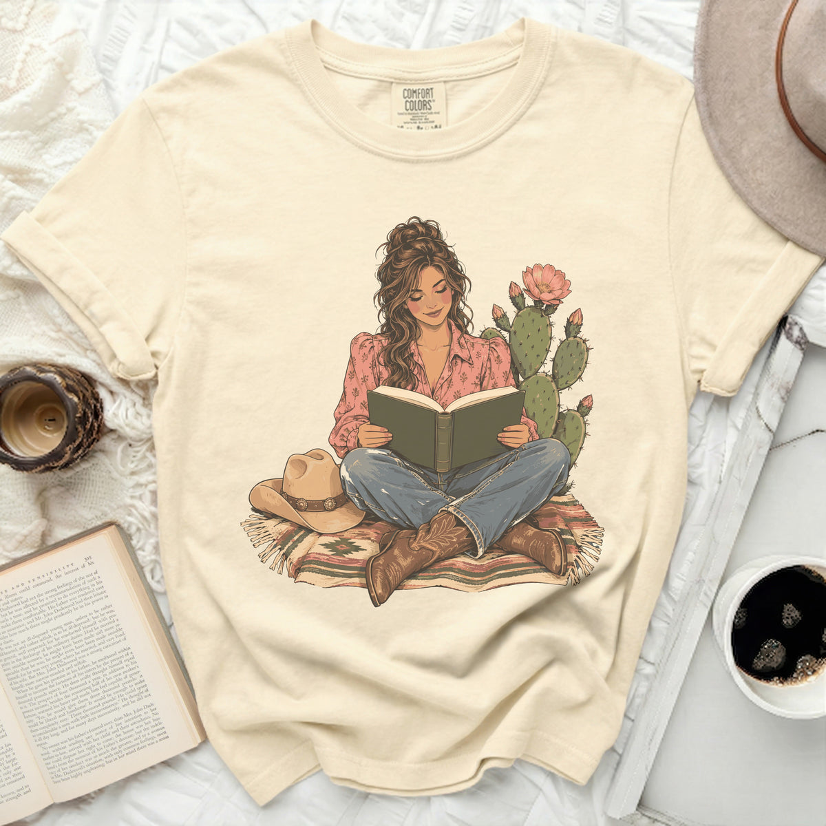 Comfort Colors t-shirt with illustration of woman reading by cactus and cowboy hat.