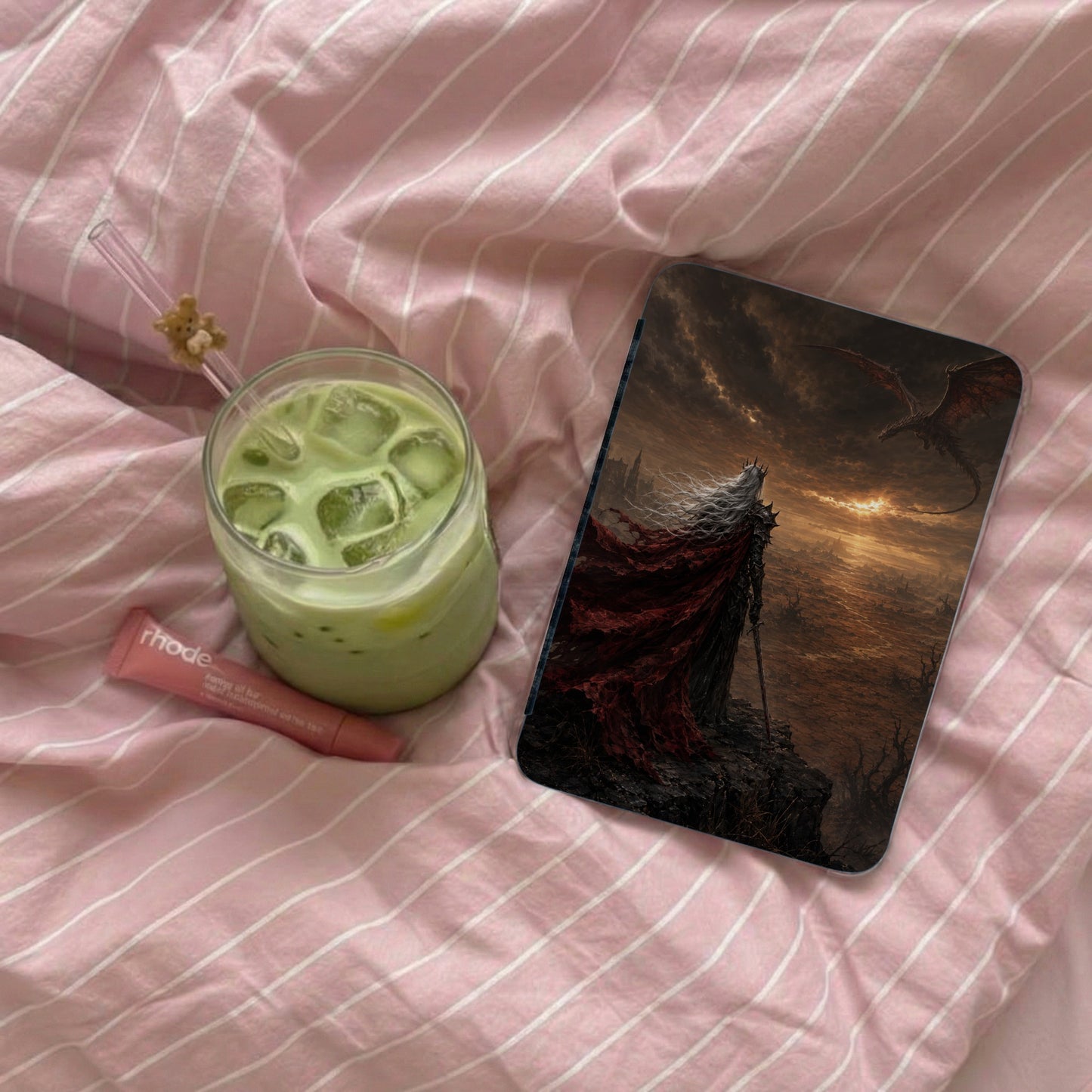 Iced green beverage and rhode lip balm next to phone case featuring a warrior and dragon.