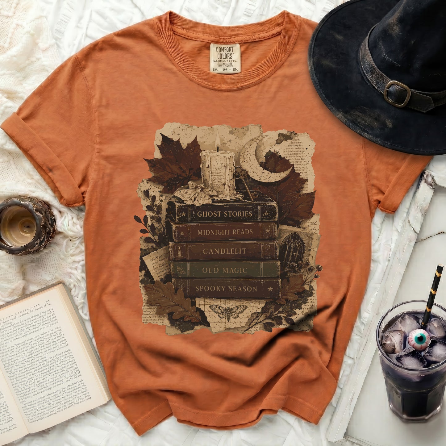 Orange t-shirt with stacked Halloween-themed books and candle graphic.