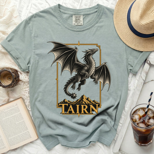 Light blue t-shirt with black dragon graphic and gold border with "TAIRN" text.