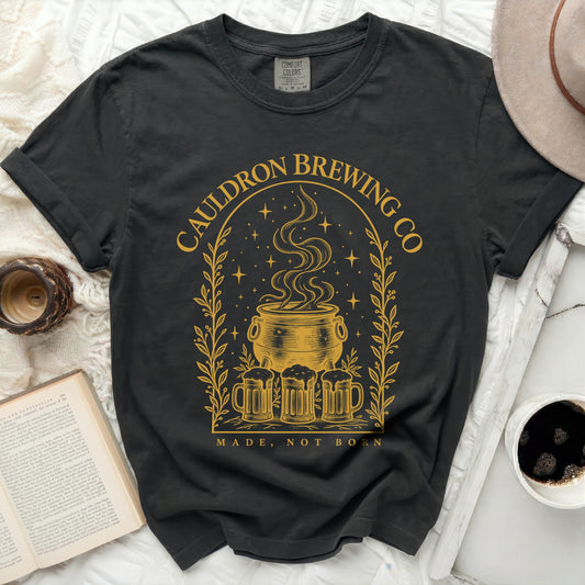 A black crewneck t-shirt featuring a gold graphic of a steaming cauldron, beer mugs, and text.