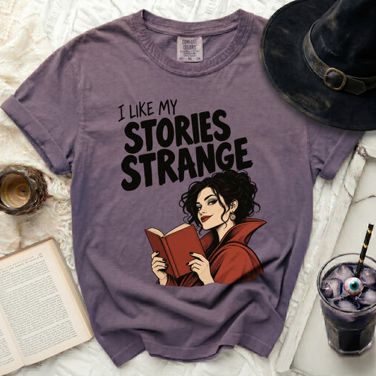 Purple t-shirt with "I LIKE MY STORIES STRANGE" and witch reading book graphic.