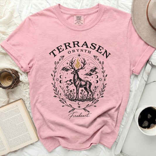 A pink t-shirt featuring a black and gold graphic of a stag surrounded by flowers, moons, clouds, and the text Terrasen and Fireheart.