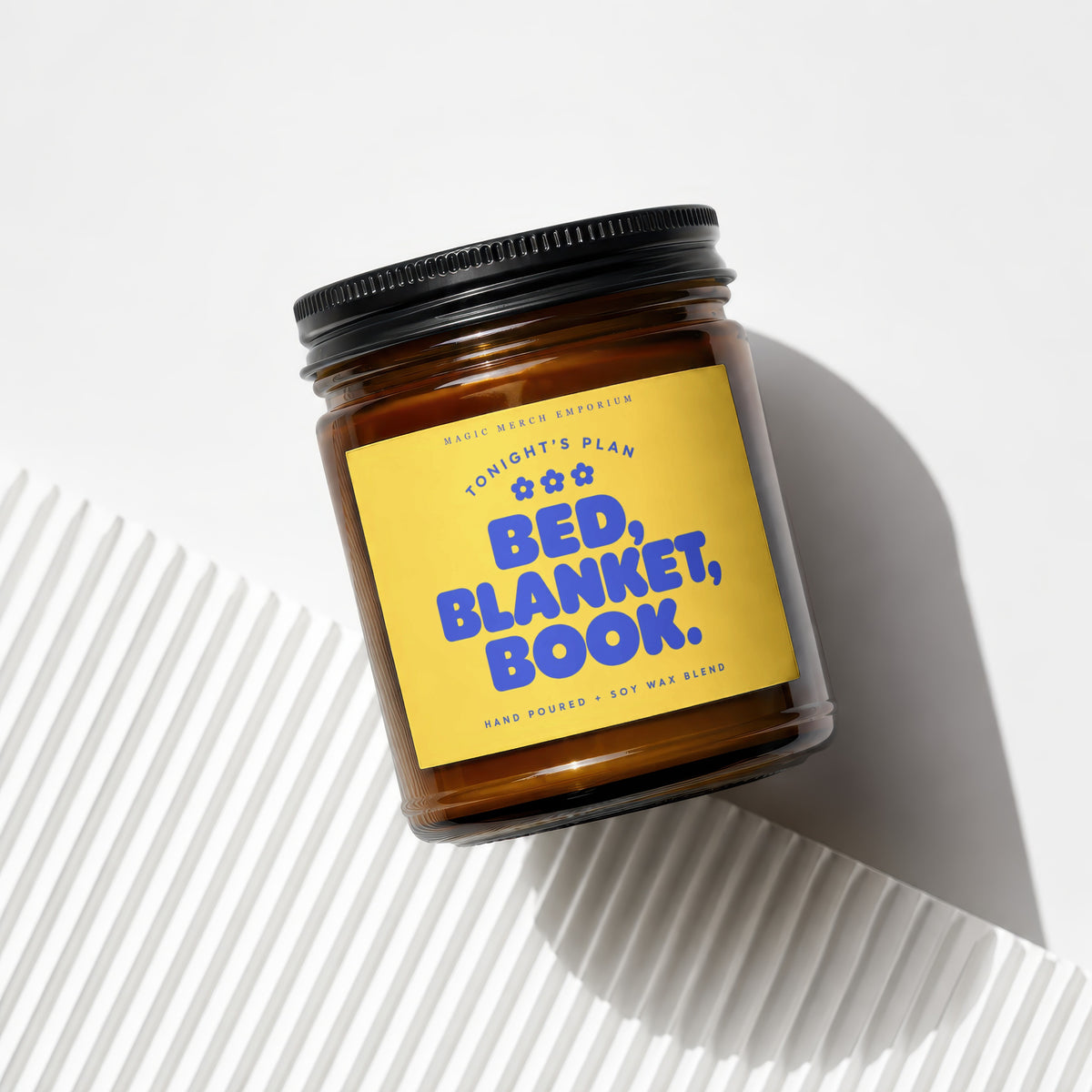 Brown glass candle with yellow label reading "Tonight's Plan Bed, Blanket, Book."