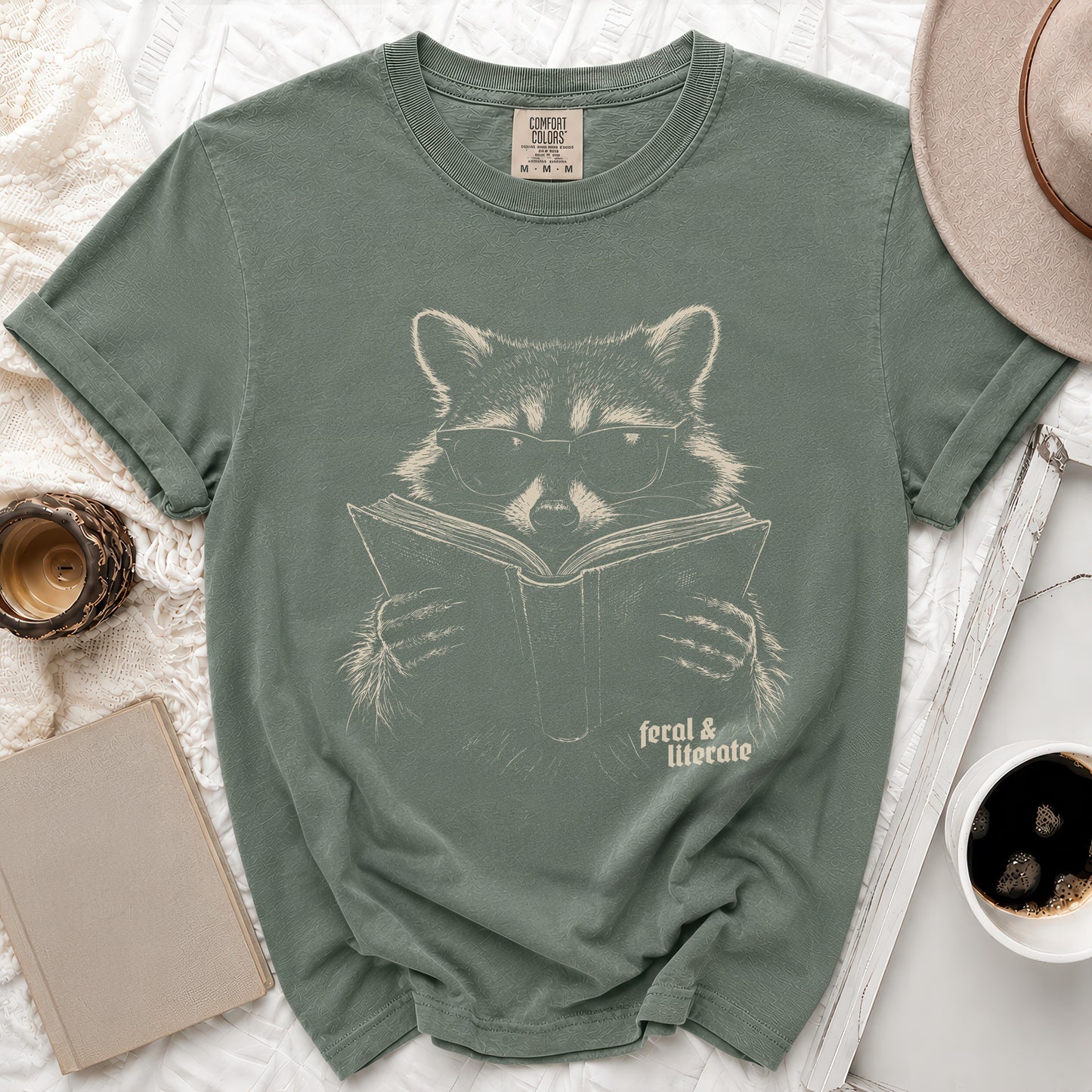 Green t-shirt with a graphic of a raccoon wearing glasses reading a book, "feral & literate" text.