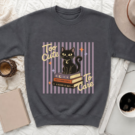 Black cat sitting on books with text "Too Cute To Care" on sweatshirt.