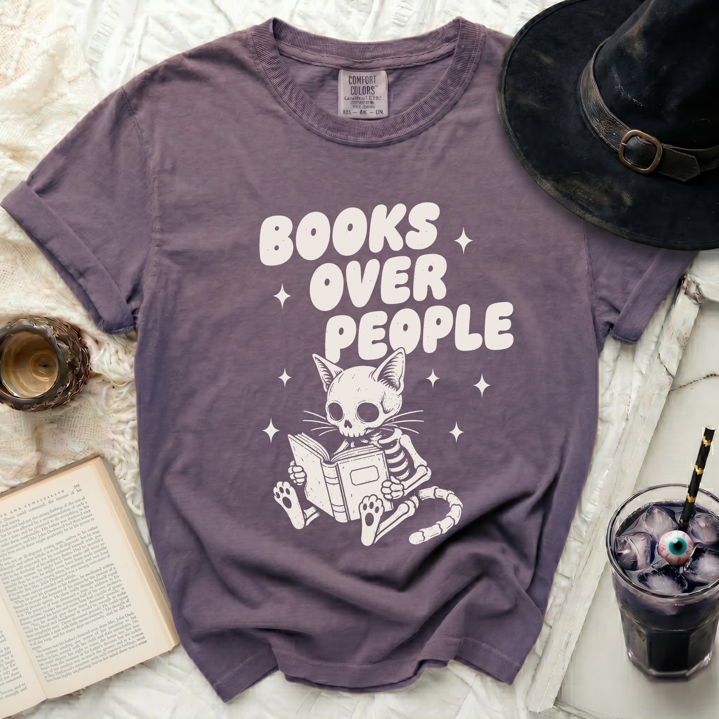 Skeleton cat reads a book with "Books over people" text.