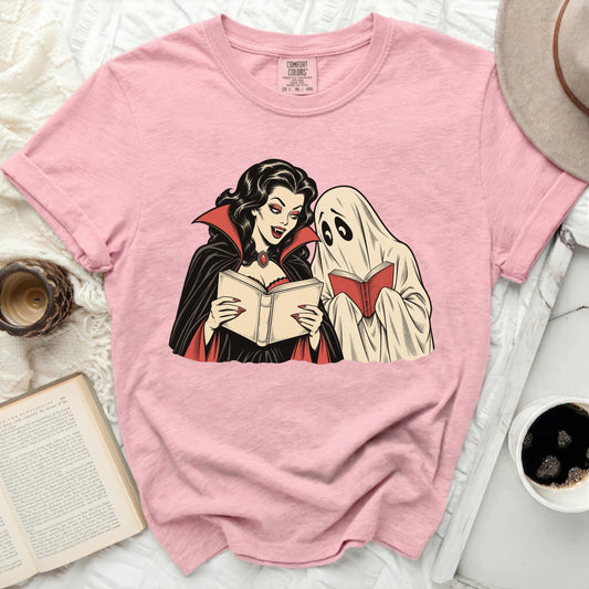 Pink t-shirt with graphic of a vampire and ghost reading books.