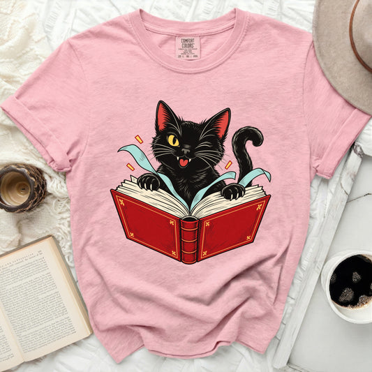 Pink t-shirt with black cat illustration reading an open red book.