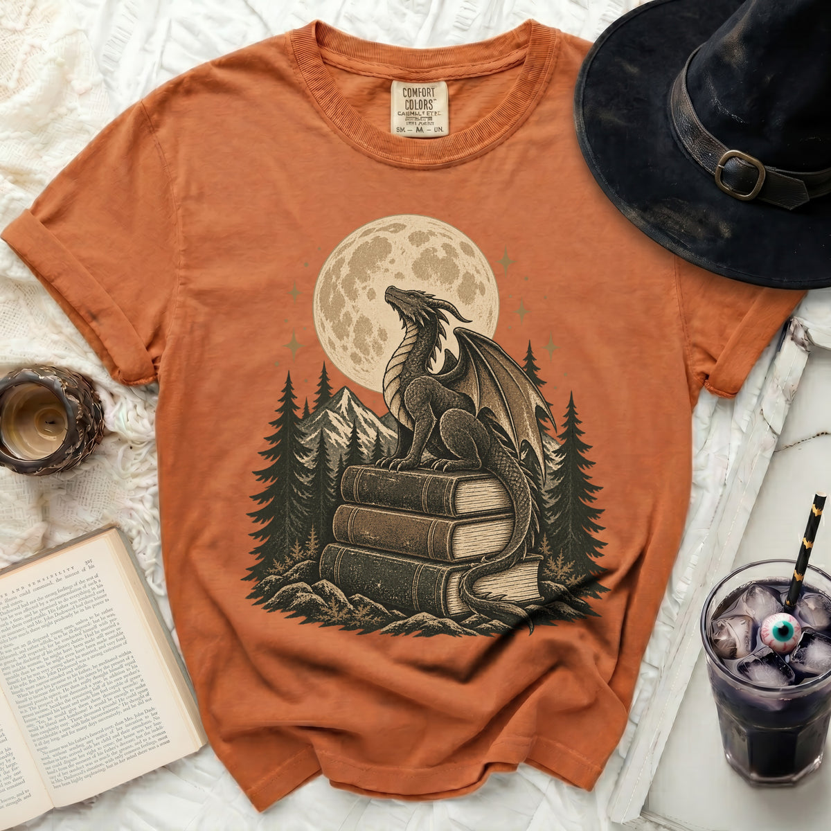 Orange t-shirt with a dragon sitting on books under a full moon.