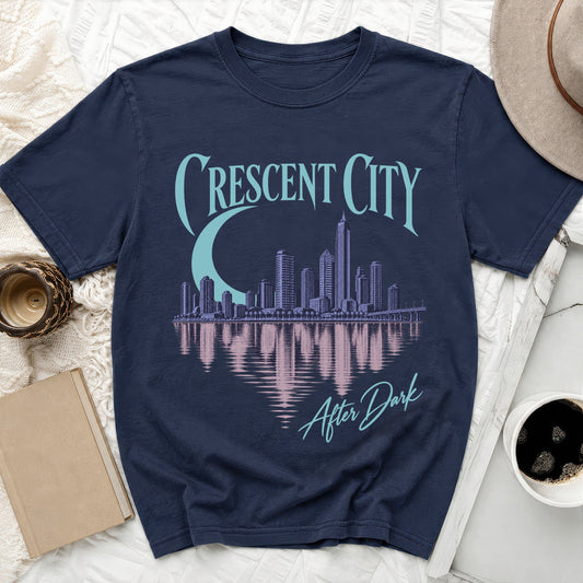 A dark blue t-shirt printed with a purple city skyline, water reflection, and Crescent City After Dark text.