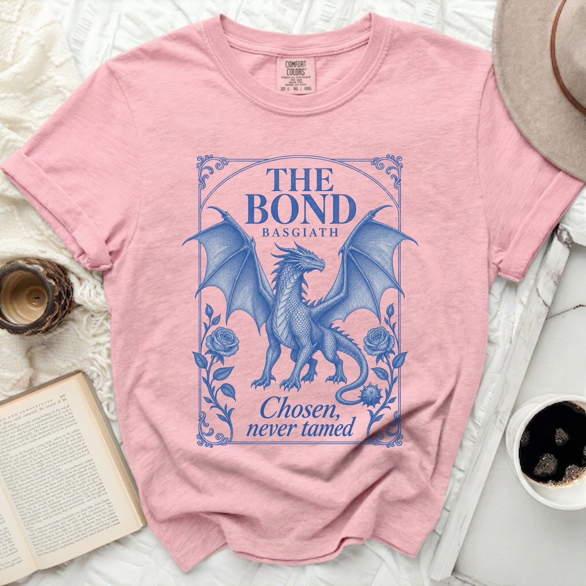 Pink t-shirt featuring a blue graphic of a winged dragon with roses and text reading THE BOND BASGIATH Chosen, never tamed.