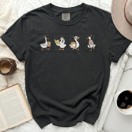 Dark t-shirt with four postage stamp illustrations of geese reading books.
