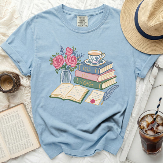 Light blue t-shirt with illustration of books, teacup, roses, ink quill, and open letter.