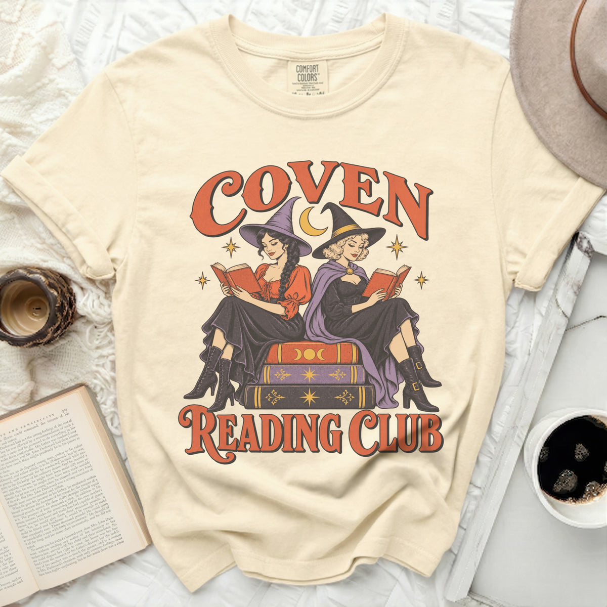 Cream t-shirt with graphic of two witches reading, text says "Coven Reading Club".