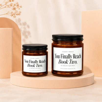 Two amber glass candle jars with black lids and white labels on a beige platform.