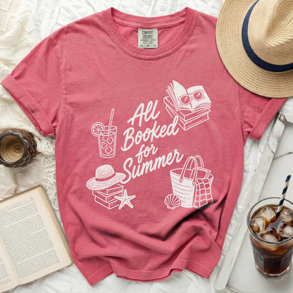 Coral t-shirt with white graphic of books, sunglasses, beach bag, and hat.