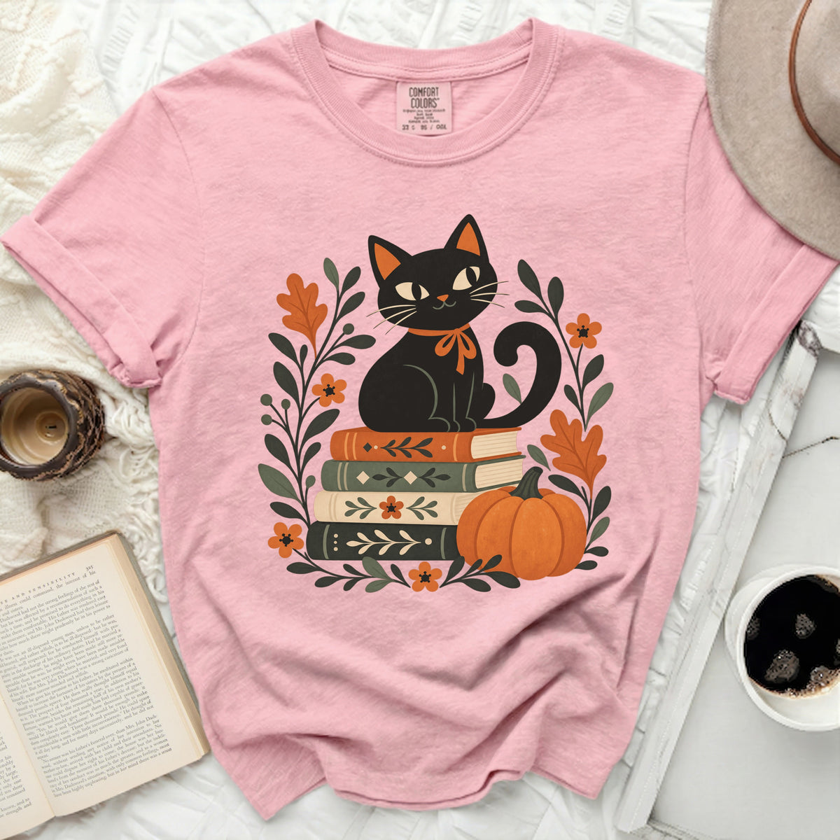 Pink t-shirt with black cat, books, pumpkin, and fall leaves graphic.