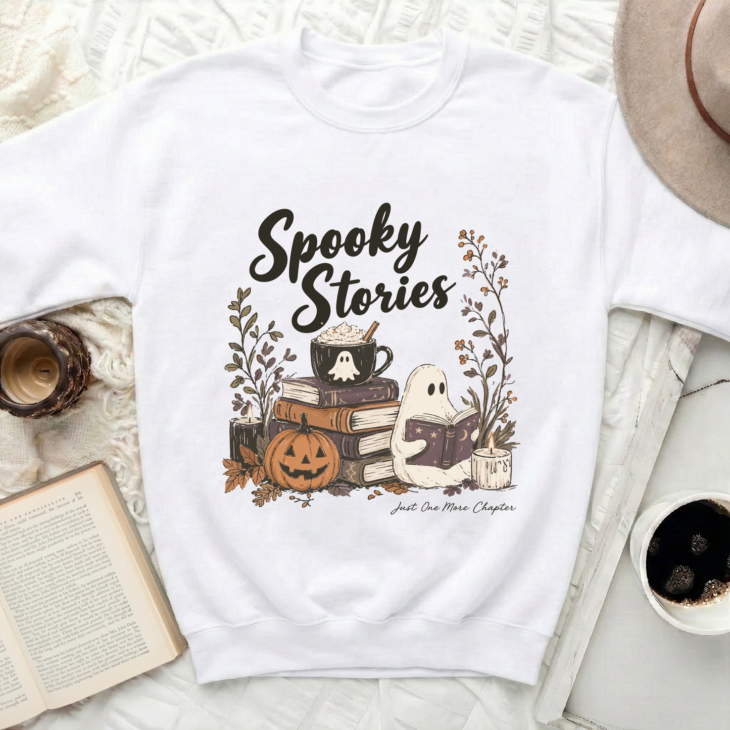 White sweatshirt with "Spooky Stories" and ghost reading among books and pumpkin.