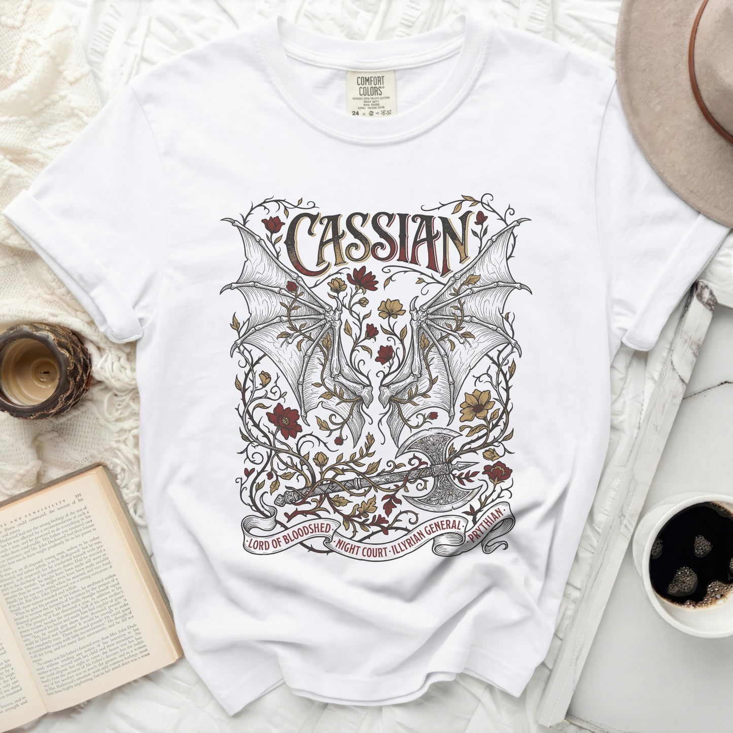 White t-shirt with a Cassian design featuring bat wings, an axe, and floral elements.