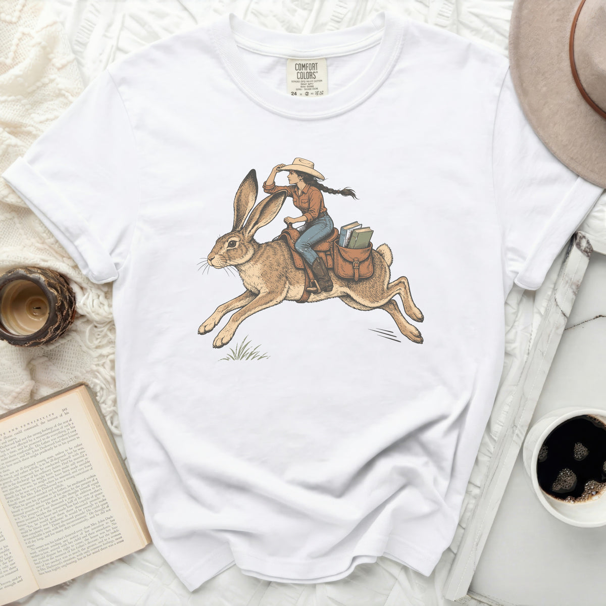 White t-shirt with illustration of woman riding a rabbit, carrying books.
