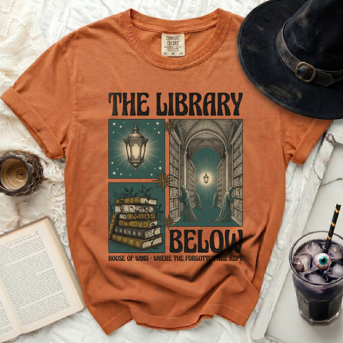 Orange t-shirt with "The Library Below" graphic featuring spooky library scenes and books.