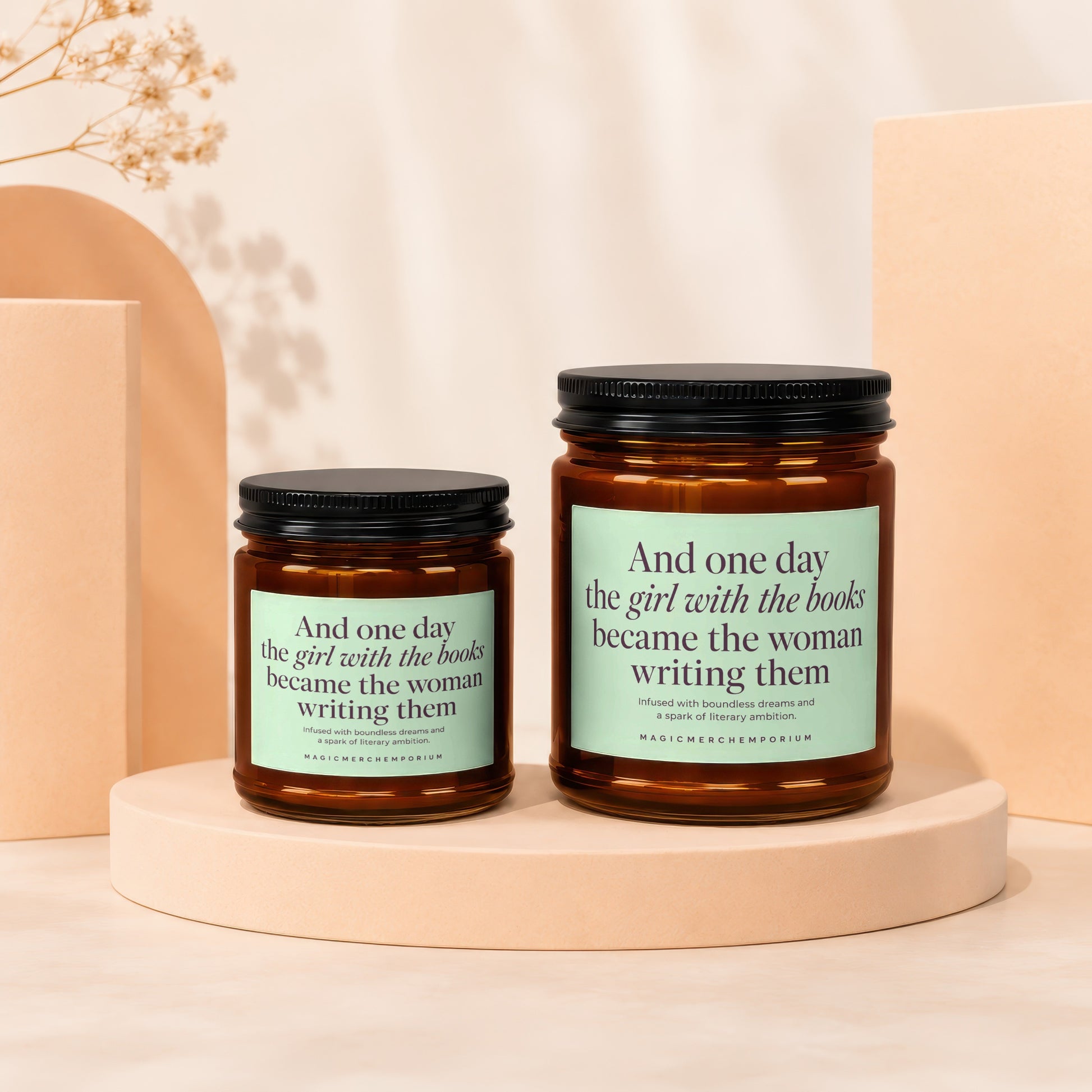 Two amber glass candles with light green labels reading "And one day the girl with the books became the woman writing them."