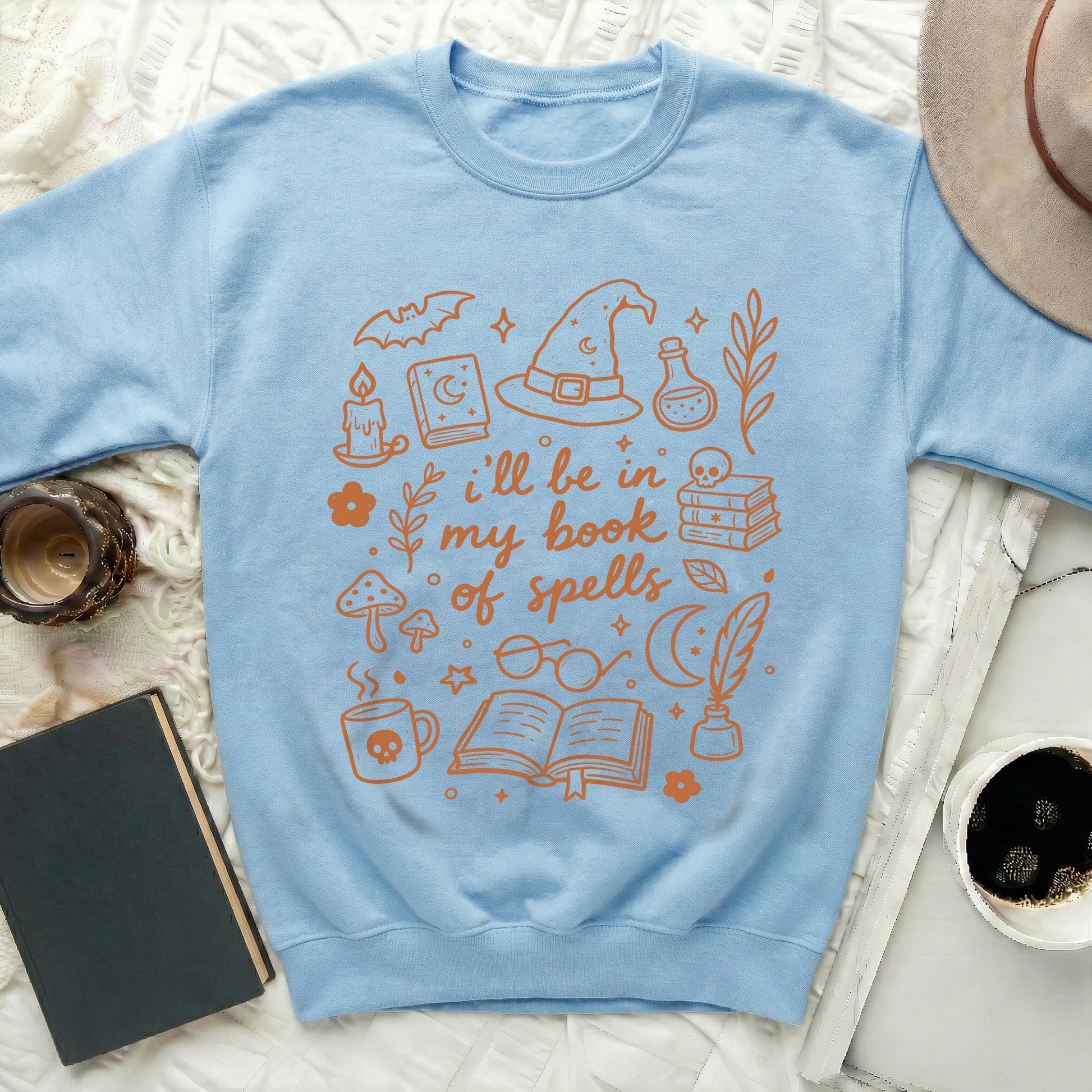 Light blue sweatshirt with orange graphic text "i'll be in my book of spells."