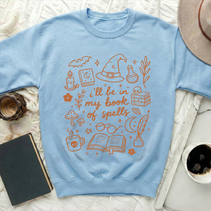 Light blue sweatshirt with orange graphic text "i'll be in my book of spells."