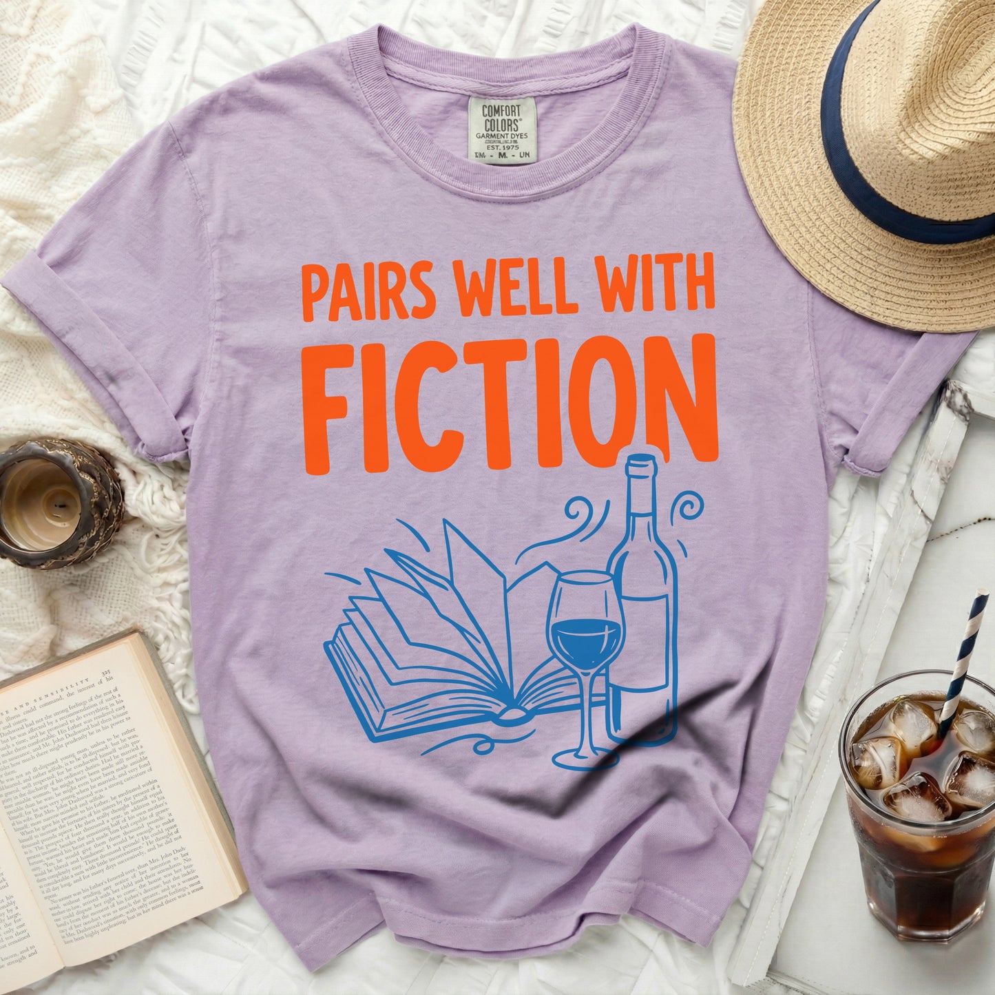 Purple t-shirt with "Pairs Well With Fiction" in orange text.