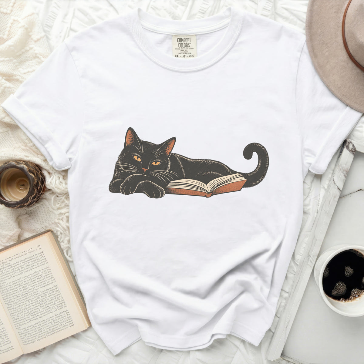 White t-shirt with a black cat illustration resting on an open book.