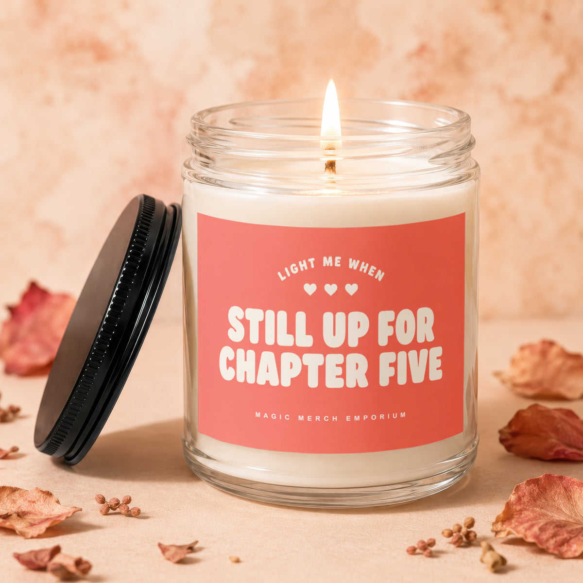 Candle with "Still Up For Chapter Five" text on pink label, lid removed.