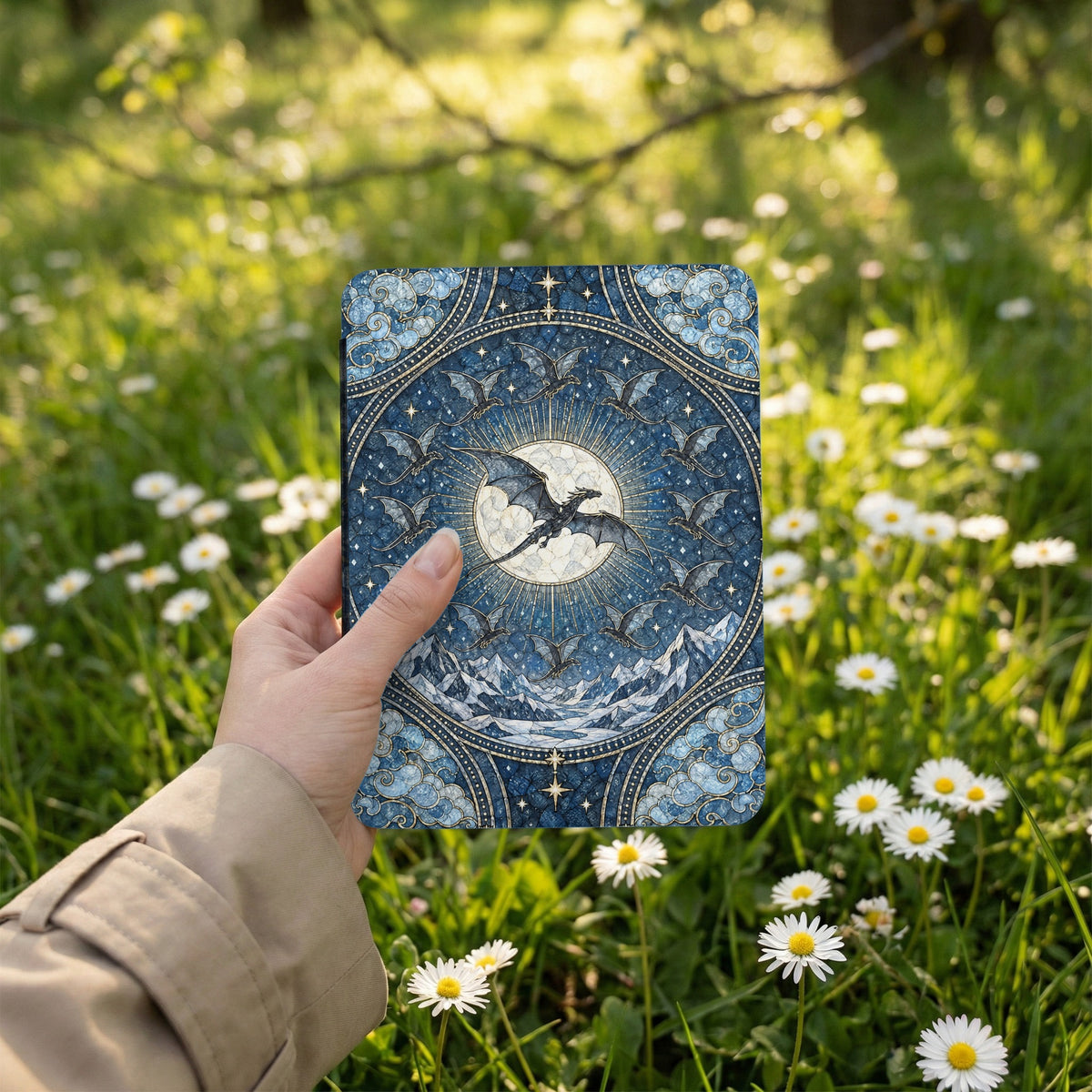 A hand holds a blue e-reader featuring a fantasy illustration of dragons circling a glowing full moon.