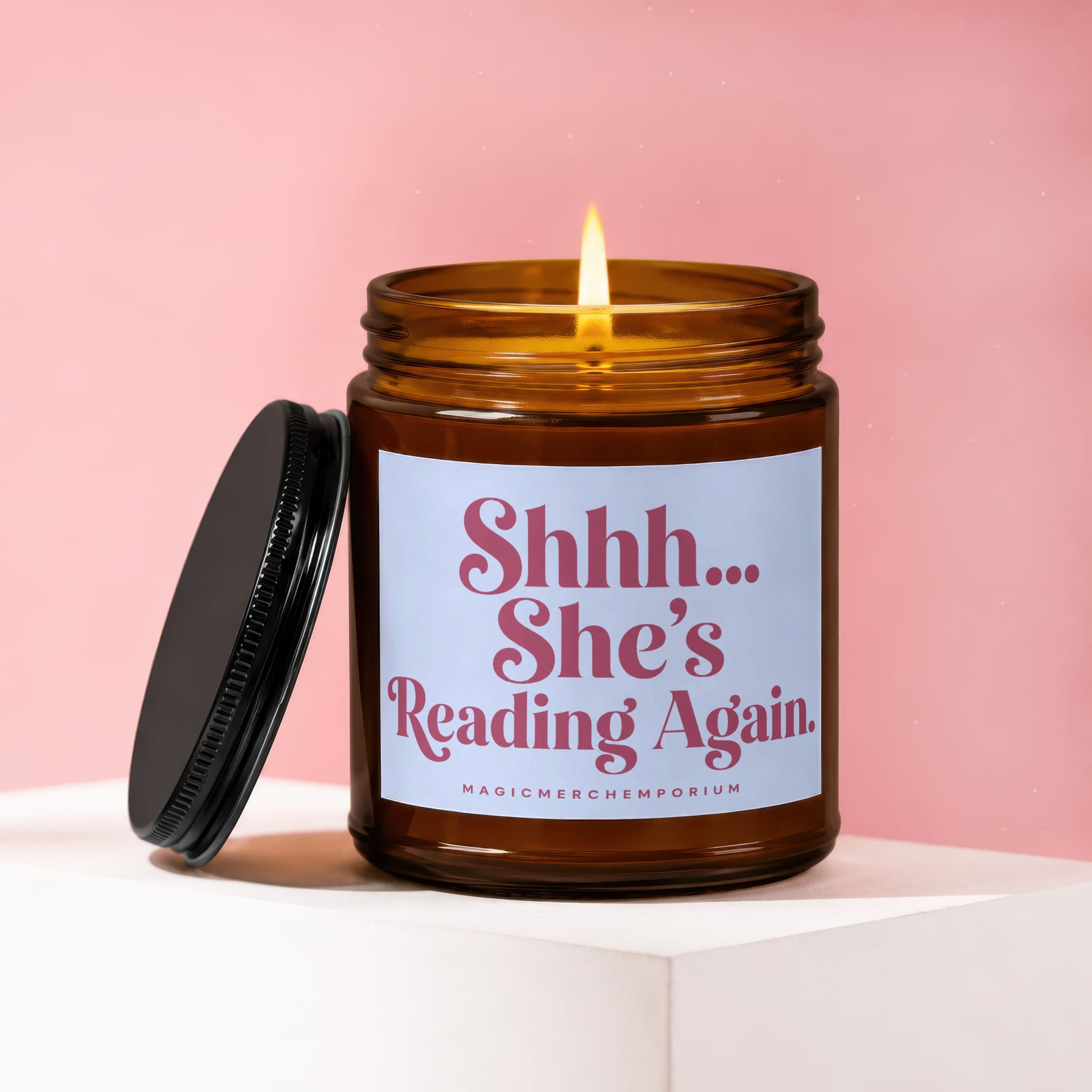 Amber candle with lit wick and lid off, showing label "Shhh... She's Reading Again."