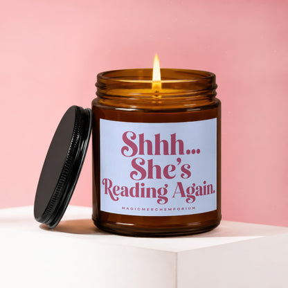 Amber candle with lit wick and lid off, showing label "Shhh... She's Reading Again."