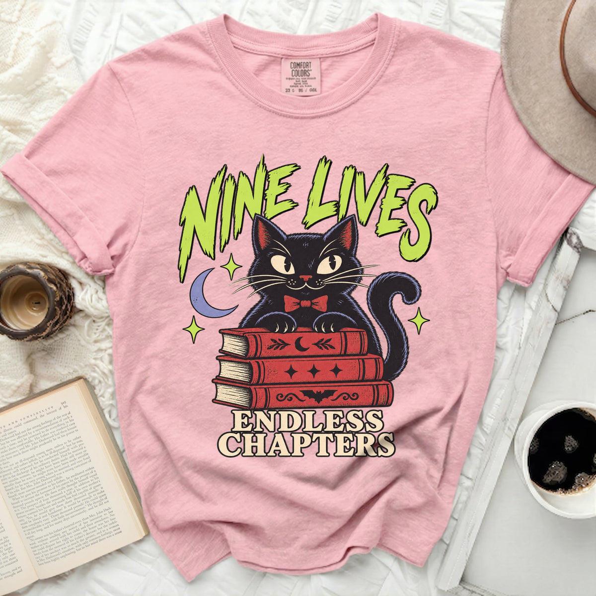 Pink t-shirt with a black cat reading books, text "NINE LIVES ENDLESS CHAPTERS".