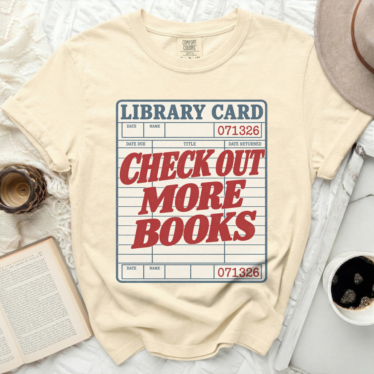 Light yellow t-shirt with a library card graphic reading "Check Out More Books."