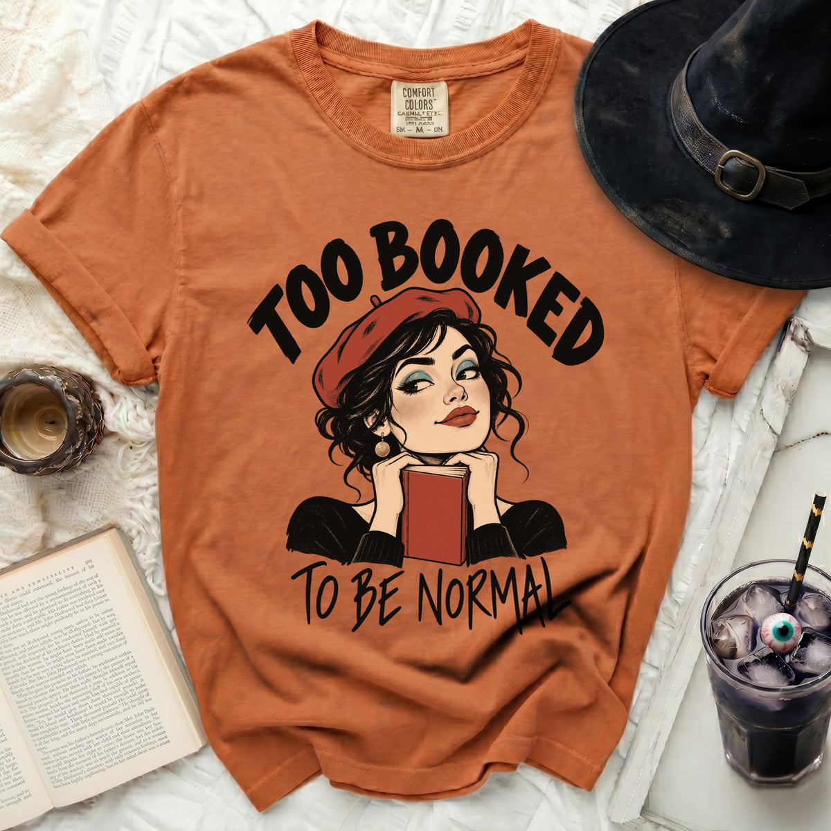 Orange t-shirt with "Too Booked To Be Normal" text and a drawing of a woman holding a book.