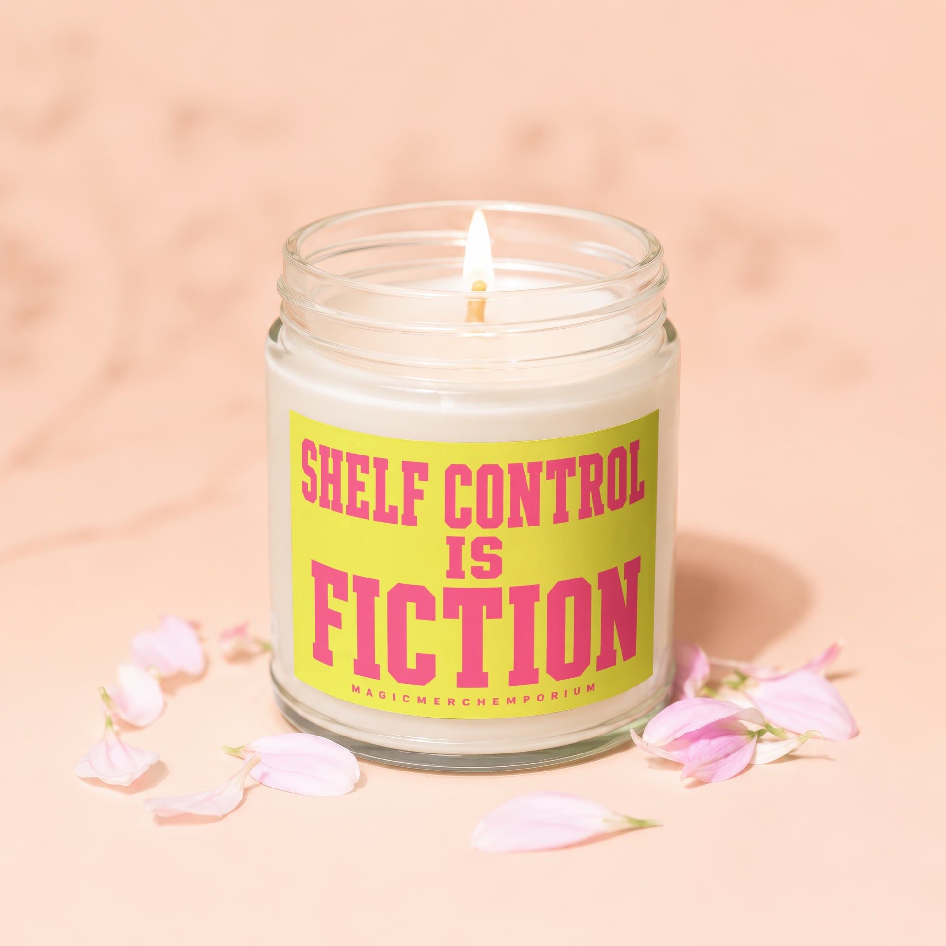 Candle with text "Shelf Control is Fiction" on a yellow label, surrounded by pink petals.