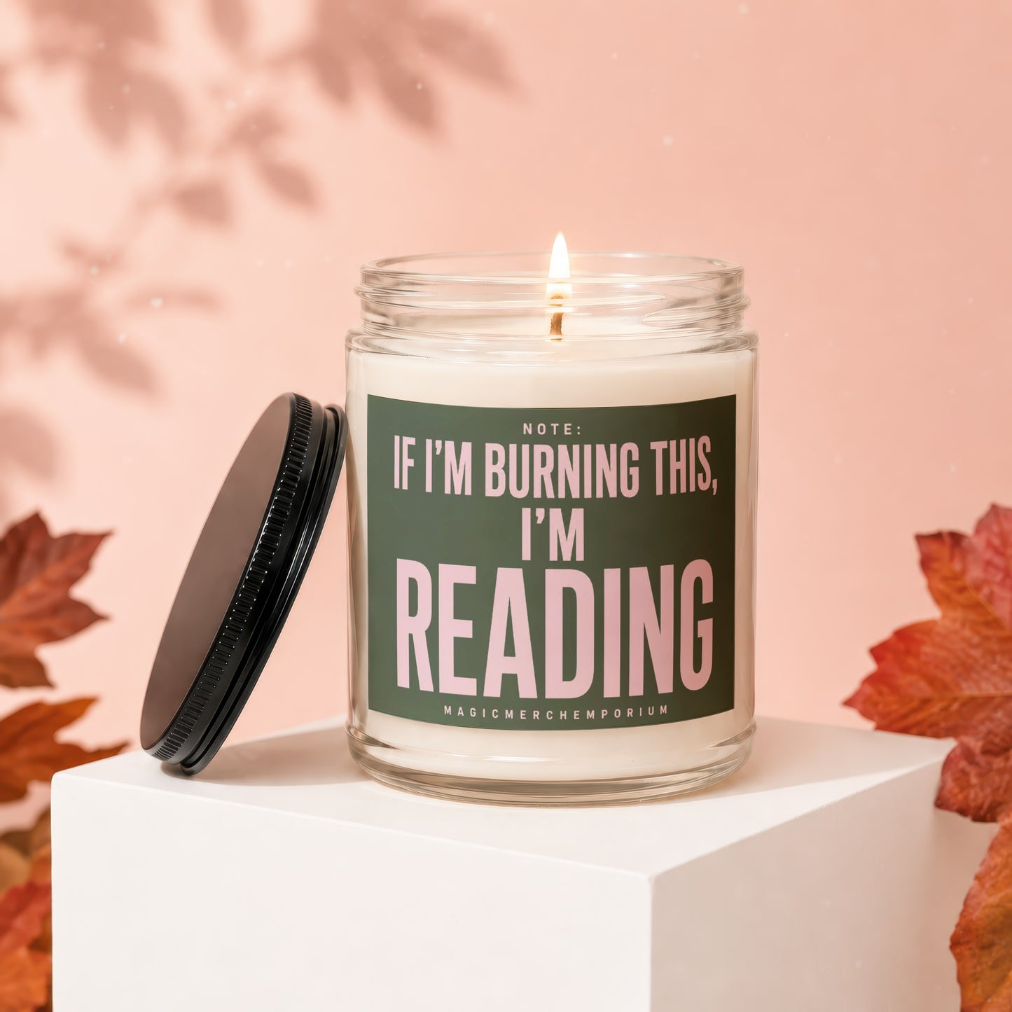 Glass candle with a lit wick and dark lid, reads "If I'm burning this, I'm reading."