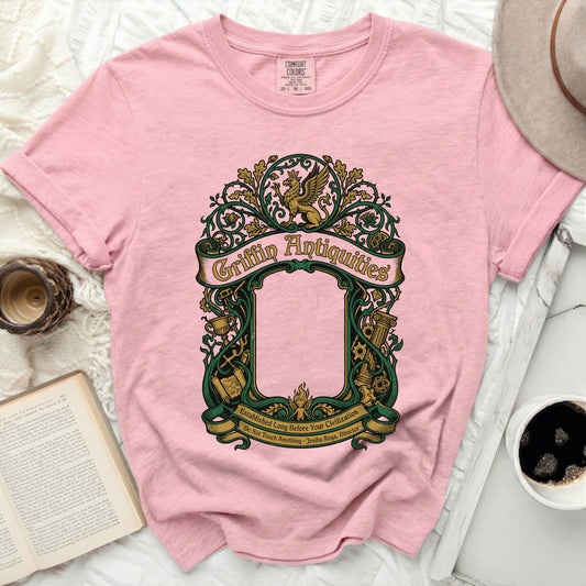 Pink t-shirt with "Griffin Antiquities" in ornate green text and a mythical creature.